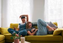 two girls lounge on a yellow couch